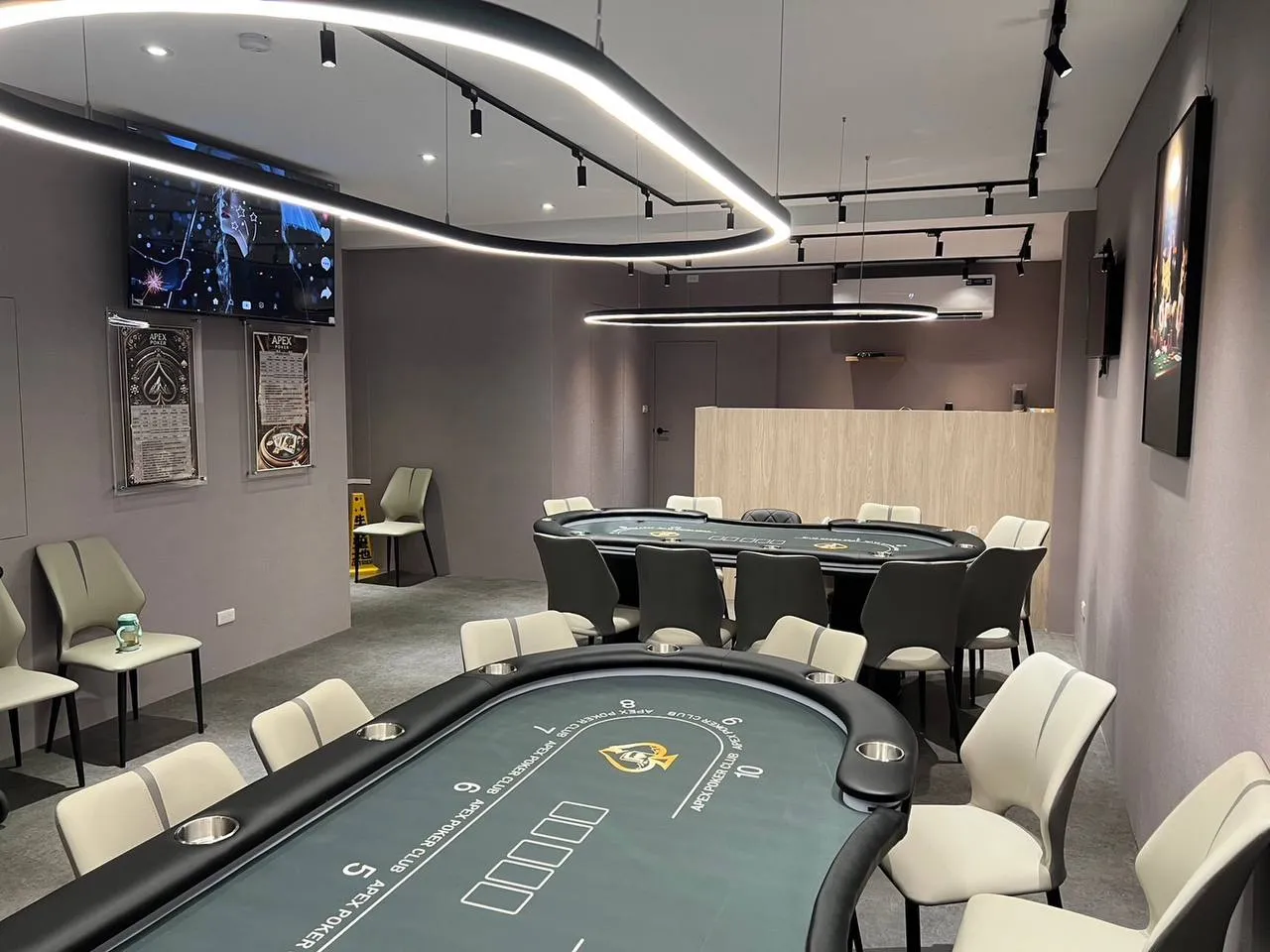Apex Poker 賽場靠櫃檯的一側，兩張牌桌與弧形燈條天花板，牆上掛著兩張黑底的說明表