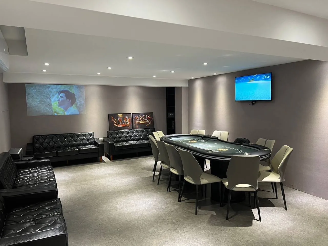 Apex Poker 的賽場一角，一張牌桌配十張米色座椅，另一側是黑色皮沙發與兩幅撲克主題畫作