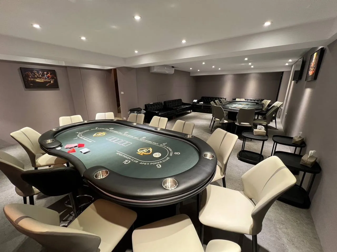 Apex Poker 賽場裡的兩張綠色牌桌，桌面印著 APEX POKER CLUB 與座位號碼，四周是米色座椅